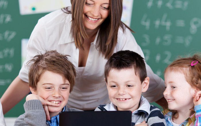 Elementary teacher supporting small group of students collaborating on laptop-based math activity